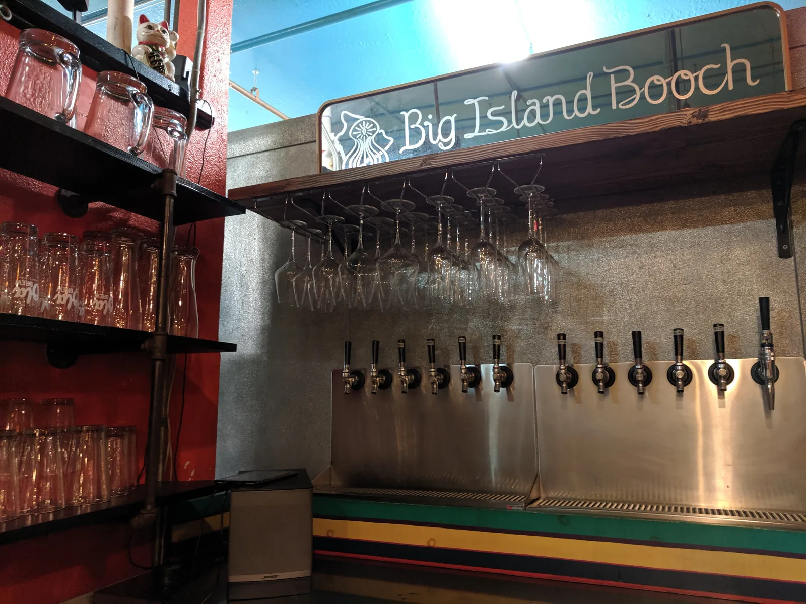 The Big Island Booch taproom tap wall with hanging glassware and a carved wooden sign.