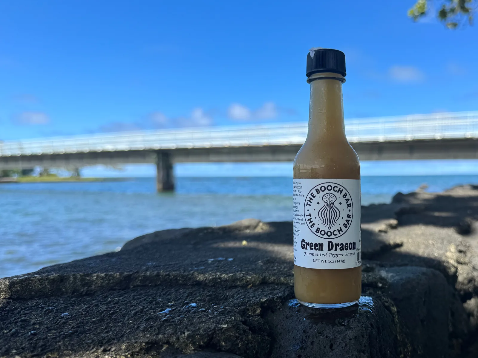 A 5 oz bottle of Big Island Booch Green Dragon fermented pepper sauce, mild, on lava rock at Hilo Bay