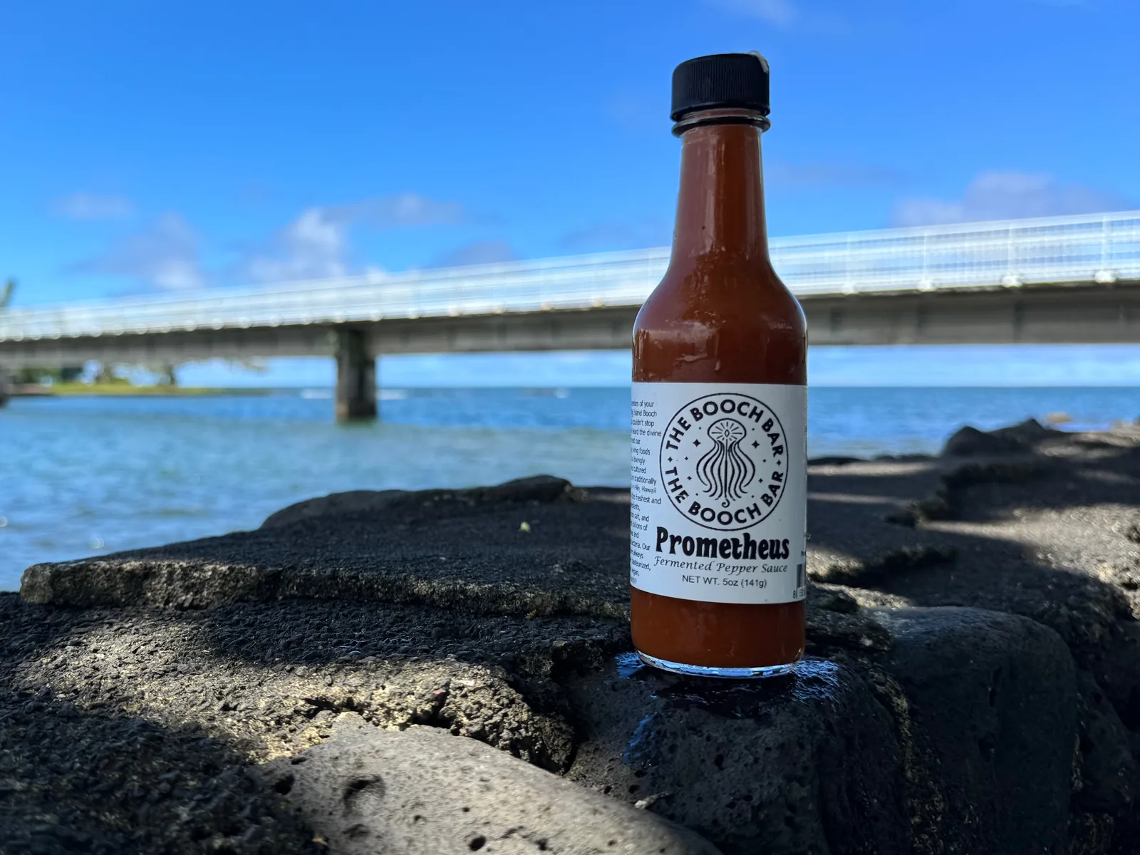 A 5 oz bottle of Big Island Booch Prometheus fermented pepper sauce, extra hot, on lava rock at Hilo Bay