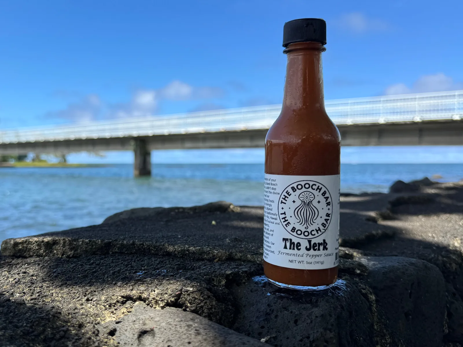 A 5 oz bottle of Big Island Booch The Jerk fermented pepper sauce, medium, on lava rock at Hilo Bay