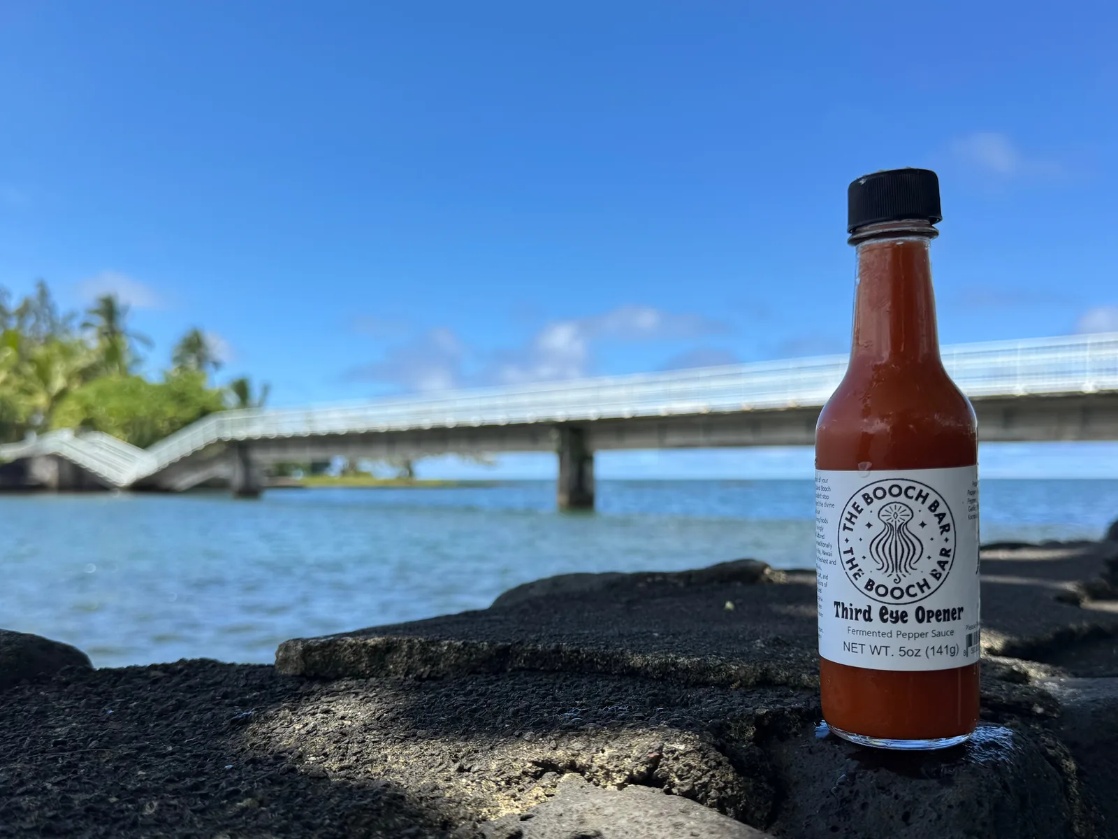 A 5 oz bottle of Big Island Booch Third Eye Opener fermented pepper sauce, hot, on lava rock at Hilo Bay